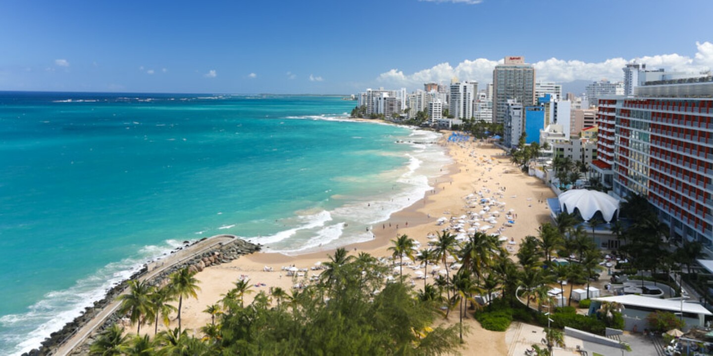 Condado Beach panoramic view showing white sand, palm trees, turquoise Atlantic water, and the San Juan hotel skyline